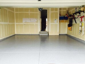 A garage with a tiled floor, a door leading to a dark interior, and various tools and equipment on the walls.