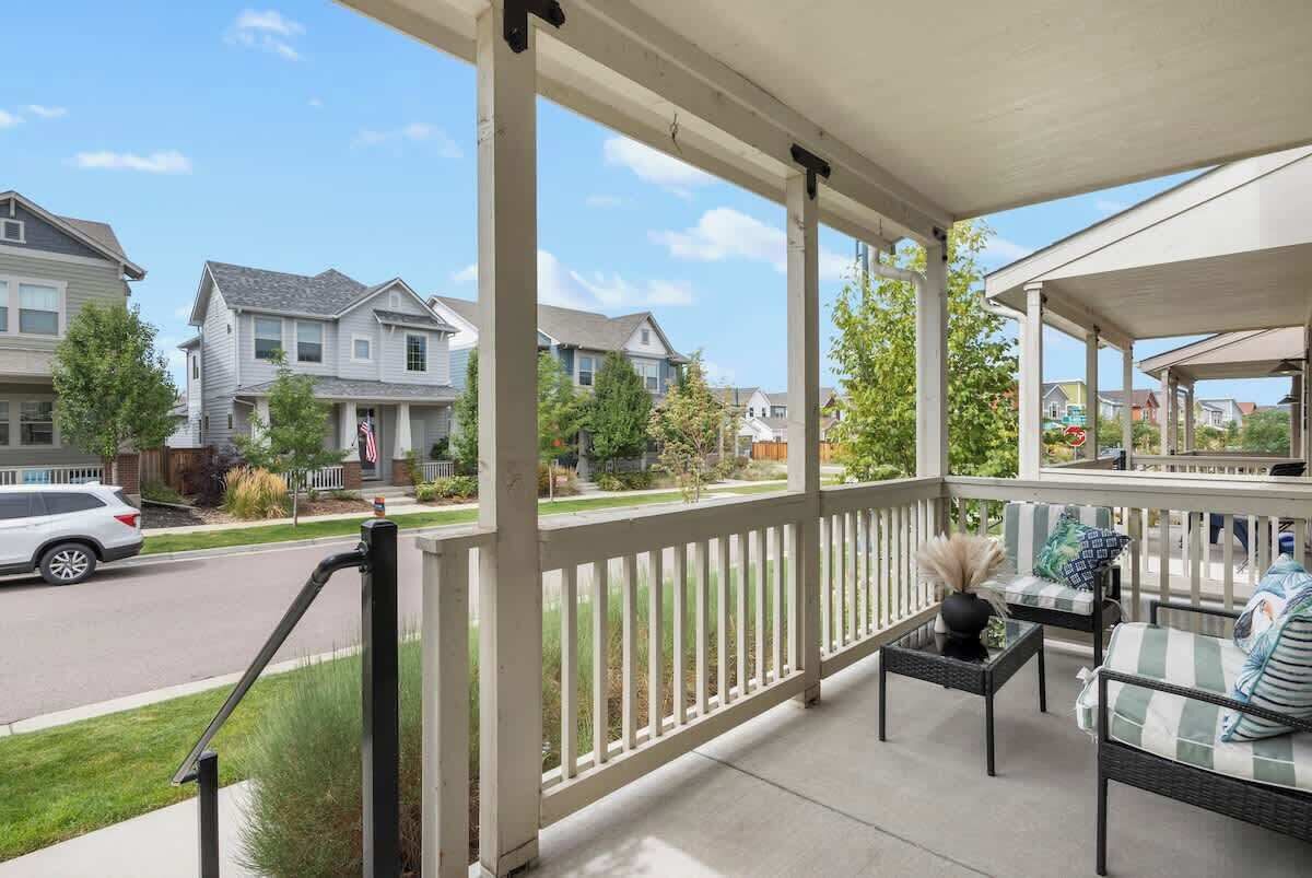 A covered porch with a railing, outdoor seating, and a view of residential houses.