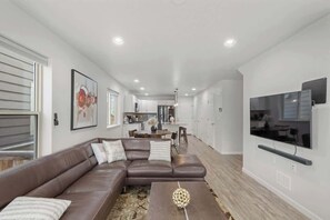 A modern living room with a sectional sofa, a coffee table, and a flat-screen TV mounted on the wall. - Charming Central Park Denver Single Family Home (Denver)