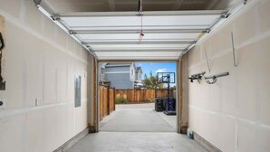 A garage with a concrete floor, a white garage door, and a view of a house and fence in the background. - Charming Central Park Denver Single Family Home (Denver)