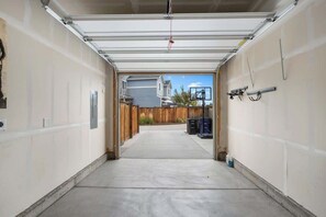 A garage with a concrete floor, a white garage door, and a view of a house and fence in the background. - Charming Central Park Denver Single Family Home (Denver)