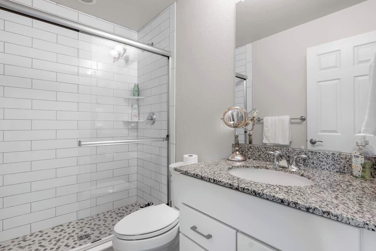A bathroom with a shower, toilet, sink, and a mirror.