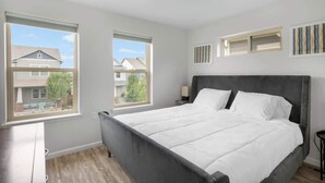 A bedroom with a large bed, two windows, a nightstand, and a wall-mounted shelf. - Charming Central Park Denver Single Family Home (Denver)