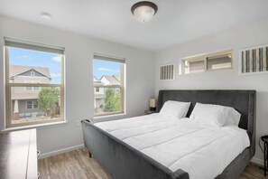 A bedroom with a large bed, two windows, a nightstand, and a wall-mounted shelf. - Charming Central Park Denver Single Family Home (Denver)