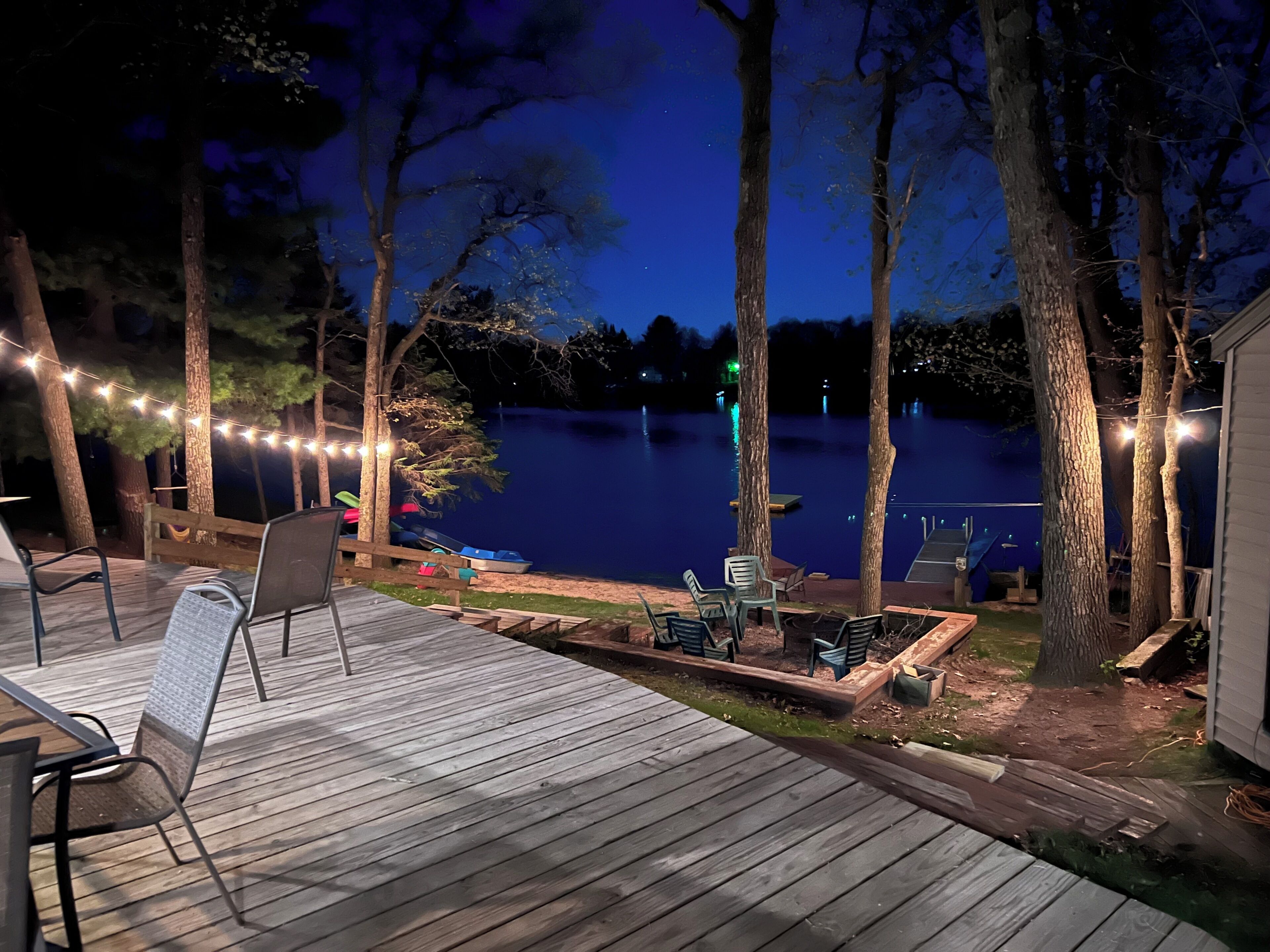 A deck with chairs and a table, overlooking a lake at night.