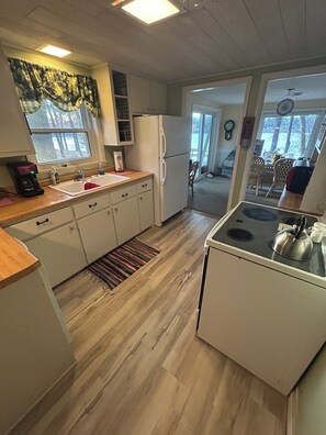 A kitchen with a refrigerator, stove, and sink. There is a window with curtains and a door leading to another room. - Lakefront Retreat Near Wisconsin Dells:  Kayak use Private Beach and Treehouse (Friendship)