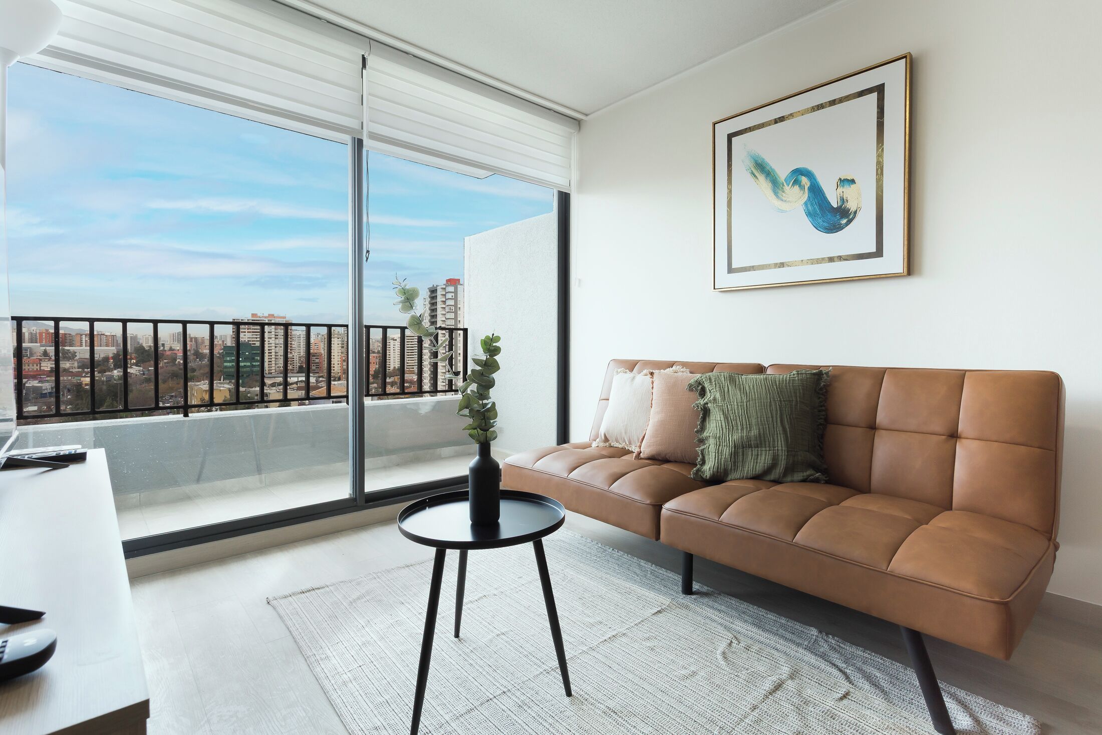 A modern living room with a leather sofa, a small round table, and a view of a cityscape through large windows.