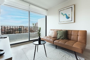 A modern living room with a leather sofa, a small round table, and a view of a cityscape through large windows.