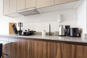 A kitchen with a granite countertop, wooden cabinets, a coffee maker, a kettle, and a knife set. - Centenario 1151 (Santiago)