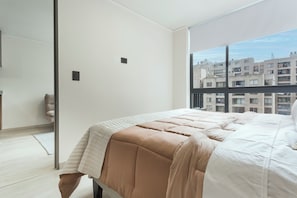 Un dormitorio moderno con una cama grande, vistas de edificios a través de la ventana y una puerta que da a otra habitación.