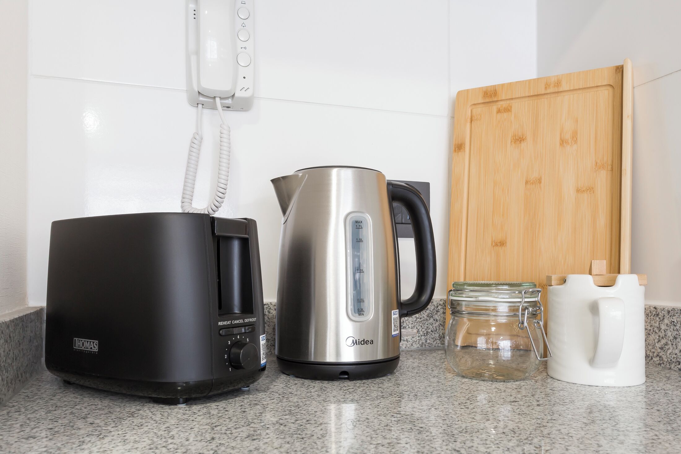 Een keuken met een koffiezetapparaat, een waterkoker, een snijplank en een pot.