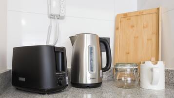 Een keuken met een koffiezetapparaat, een waterkoker, een snijplank en een pot.
