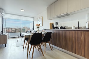 A modern kitchen with a dining area, large windows, and a city view.