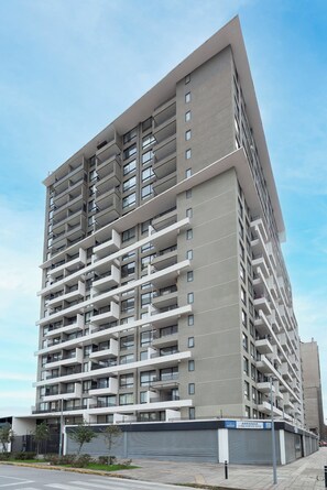 A multi-story residential building with balconies, a gated entrance, and a clear sky.