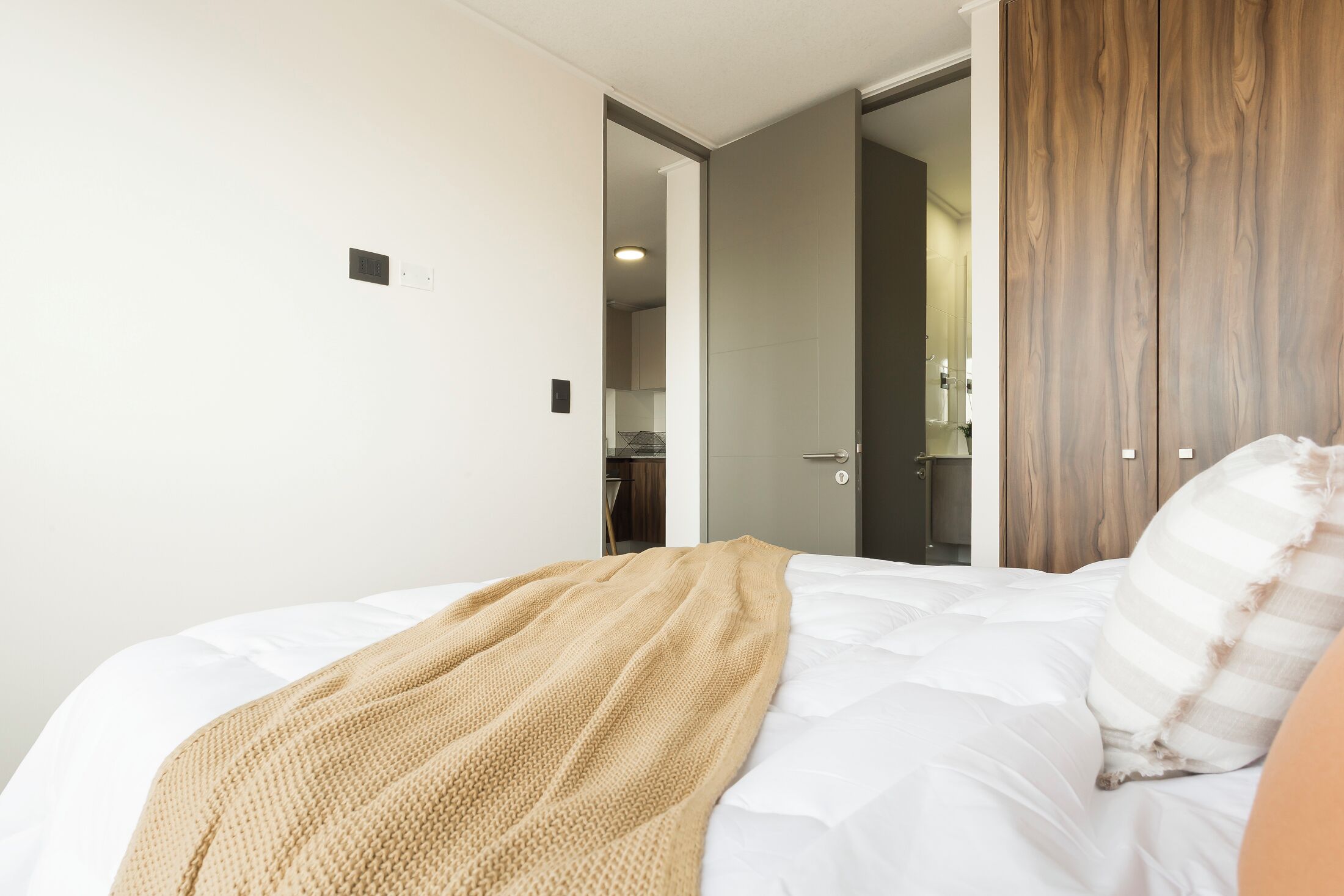 A bedroom with a bed, a wooden wardrobe, and a door leading to a bathroom.