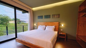 A modern bedroom with a large bed, a wooden headboard, a nightstand, and a view of greenery outside. - Narin Retreat (Zeta trece)