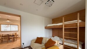 Ett litet rum med en våningssäng, en soffa med kuddar, ett matbord och en projektor som är monterad i taket.