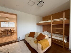 Une pièce compacte comprenant un lit superposé, un canapé avec des coussins, une table à manger et un projecteur fixé au plafond.