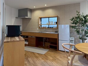 Una cocina compacta con estufa integrada, ventana con persianas, un lavabo y una zona de comedor con mesa y sillas.