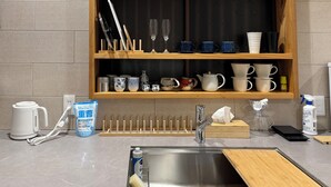 Ett kök med en trähylla där olika sorters koppar står och ett handfat med en skärbräda.