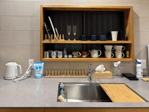Une cuisine avec une étagère en bois où sont rangées différentes tasses et un évier avec une planche à découper.