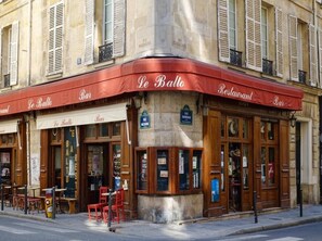 Un restaurant avec un auvent rouge, des tables en terrasse et une façade en pierre.