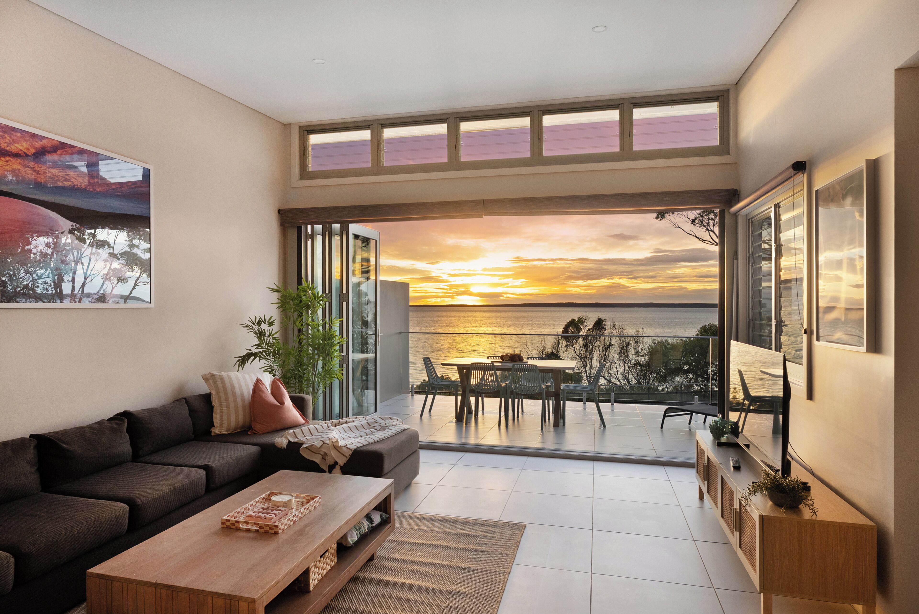 Ein modernes Wohnzimmer mit einer Couch, einem Couchtisch und Blick auf den Sonnenuntergang über dem Wasser.