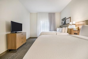 A hotel room with a bed, a TV on a wooden cabinet, a nightstand with lamps, and a window with curtains.