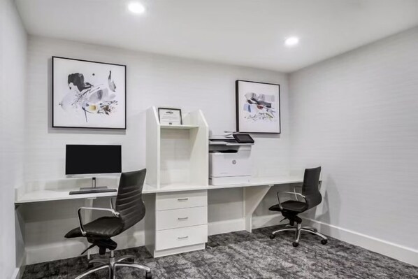 A modern office space with two desks, chairs, a printer, and framed artwork on the walls.