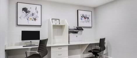 Un espace de bureau moderne comprenant deux bureaux, des chaises, une imprimante et des œuvres d’art encadrées accrochées aux murs.