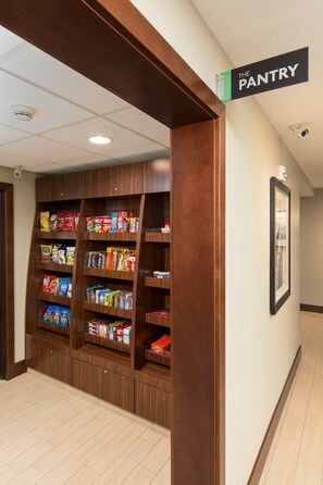 A hallway with a wooden pantry shelf stocked with snacks and beverages.