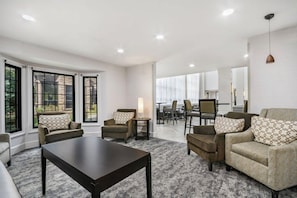 A modern living room with a sofa, armchairs, a coffee table, and a dining area in the background.