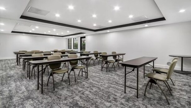 A conference room with multiple tables and chairs, a carpeted floor, and recessed ceiling lighting.