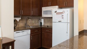 A kitchen with wooden cabinets, a microwave, a refrigerator, a dishwasher, and a granite countertop.