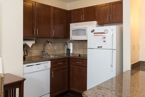 Una cocina con gabinetes de madera, microondas, refrigerador, lavavajillas y encimera de granito.