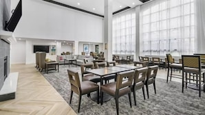 A spacious hotel dining area with multiple tables and chairs, a fireplace, and large windows.