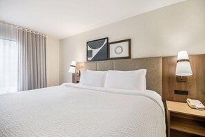 Ein Hotelzimmer mit einem großen Bett, zwei Nachttischen, einer Kopfteil und einem Fenster mit Vorhängen.
