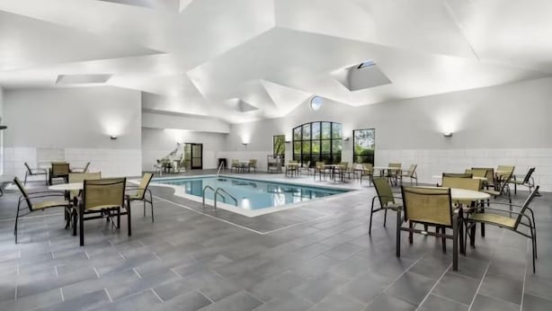 Et moderne poolområde indendørs med et geometrisk loftdesign, omgivet af spiseborde og stole.