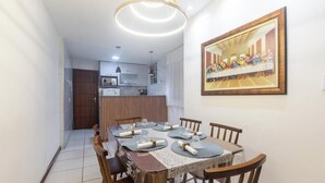 A dining area with a table set for four, a kitchen in the background, and a framed artwork on the wall. - 2-bedroom Apt 150m From the Beach Tib0103 (Guarapari)
