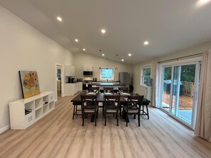 A modern kitchen with white cabinets, a dining area with dark wooden chairs, and a large window with a view of the outdoors. - Maitland Inlet Cottage — Where Goderich Sunsets, Beach Days, and Waterviews Meet (Goderich)