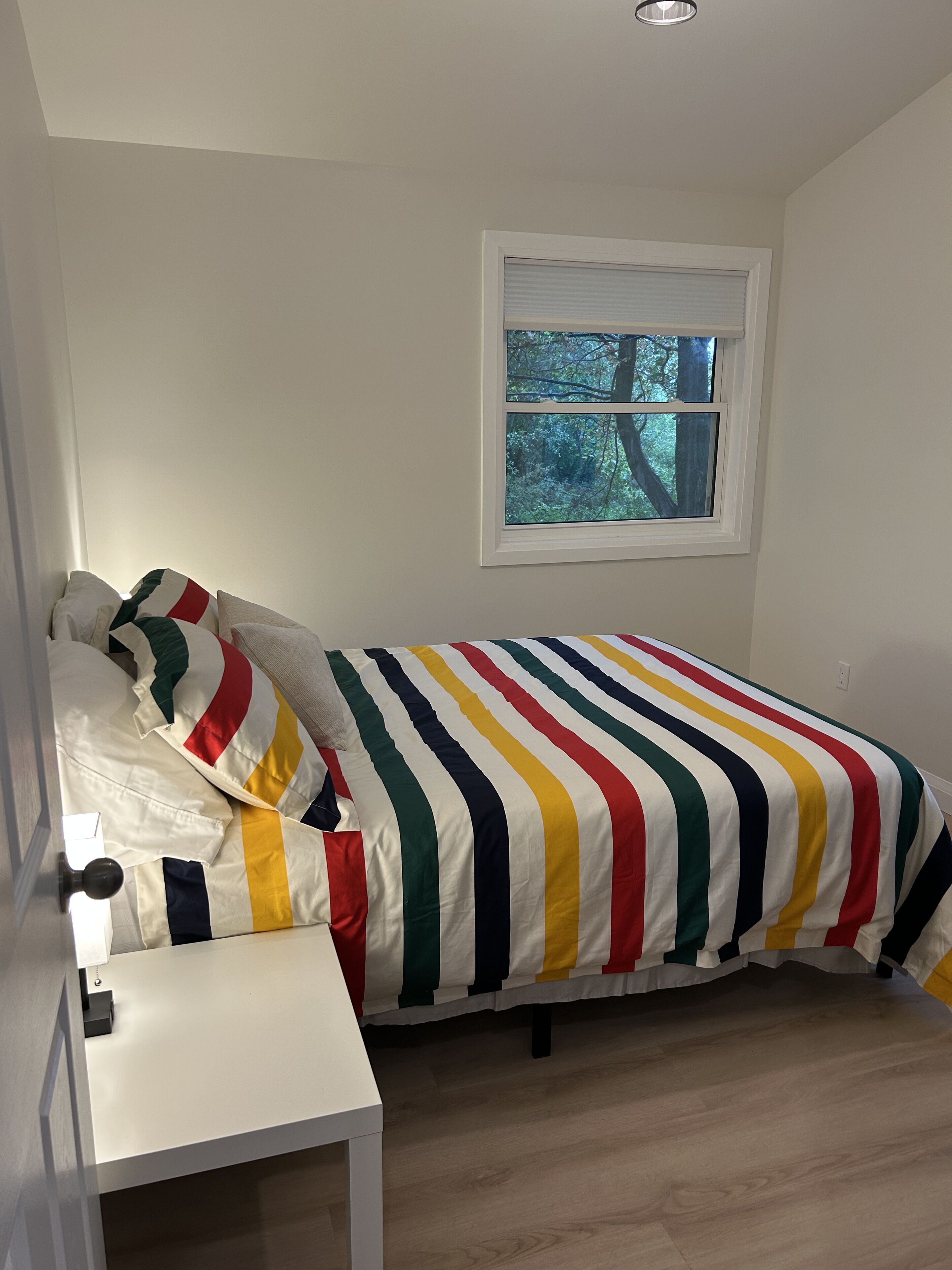 A bedroom with a single bed, a small bedside table, and a window with a view of trees.