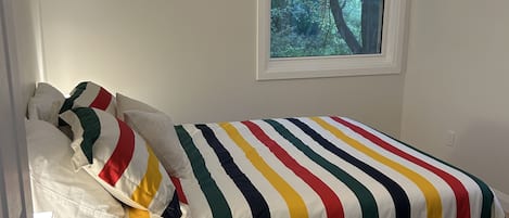 A bedroom with a single bed, a small bedside table, and a window with a view of trees.