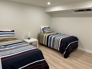 A bedroom with two single beds, a bedside table with a lamp, and a small white nightstand. - Maitland Inlet Cottage — Where Goderich Sunsets, Beach Days, and Waterviews Meet (Goderich)