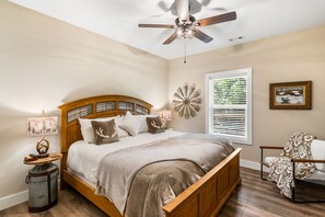 A bedroom with a wooden bed, a ceiling fan, a wall-mounted heater, and a window with blinds. - Escape to Pop's Porch, a brand-new mountain cabin (Brasstown)