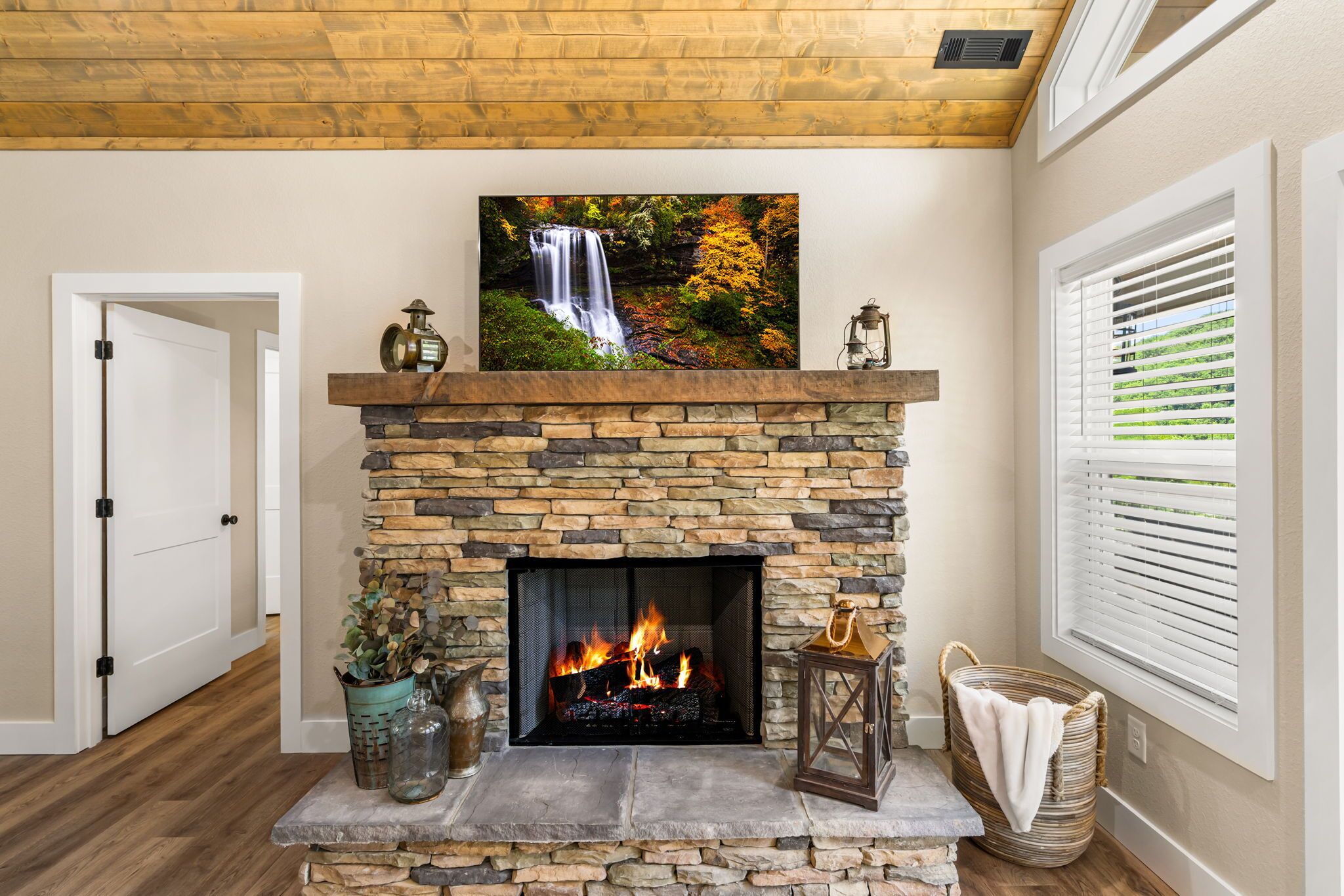 A stone fireplace with a fire, a waterfall painting above it, and a door to the left.