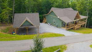 Een chalet met een overdekte veranda en een aparte garage, omgeven door bebossing.
