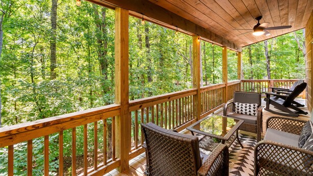 Un terrazzo in legno con mobili in vimini e un tavolo in vetro, affacciato su una foresta.