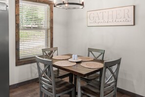 A dining area with a wooden table, four chairs, and a wall-mounted sign that reads 'GATHER with grateful hearts'. - Peaceful Seasons – A Cozy Mountain Retreat with Modern Comforts (Murphy)