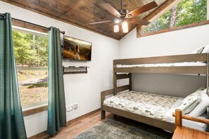 A bedroom with a bunk bed, a ceiling fan, a TV mounted on the wall, and a window with curtains. - Peaceful Seasons – A Cozy Mountain Retreat with Modern Comforts (Murphy)