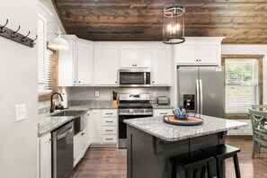 A modern kitchen with white cabinets, stainless steel appliances, and a granite countertop island. - Peaceful Seasons – A Cozy Mountain Retreat with Modern Comforts (Murphy)